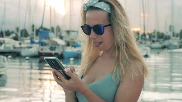 En flicka skriver på en telefon medan du vilar i hamnen. — Stockvideo