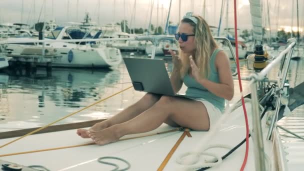 Videochat, concepto de videollamada. Una chica de videollamadas utilizando un ordenador portátil mientras está sentado en un yate . — Vídeos de Stock