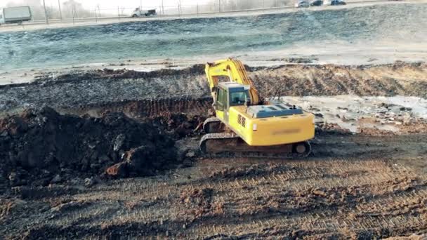 Экскаватор копает землю рядом с автомагистралью — стоковое видео