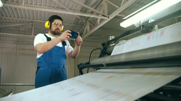 Técnico masculino está tomando fotos de una máquina de transporte de papel — Vídeos de Stock