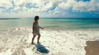 Umursamaz kadın dalgaların çekildiği kıyıda yürüyor