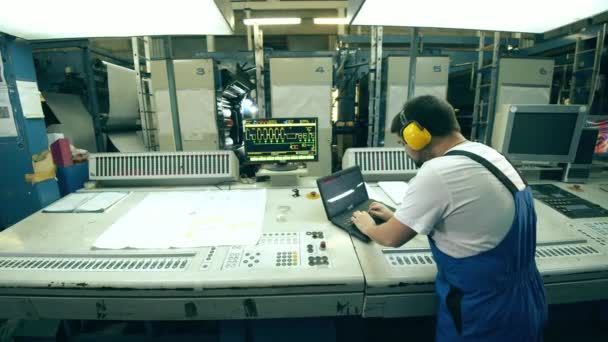 Εργάτης σε εργοστάσιο με φορητό υπολογιστή που λειτουργεί με τυπογραφικό εξοπλισμό — Αρχείο Βίντεο