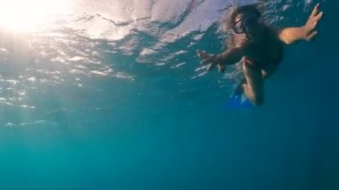 Bir kadın suyun altında yüzüyor ve kameraya bakıyor.