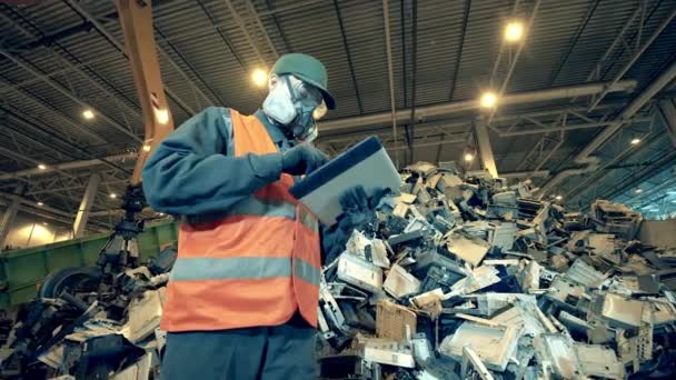 Ein Müllhaufen und ein männlicher Arbeiter mit einer Tablette daneben — Stockvideo