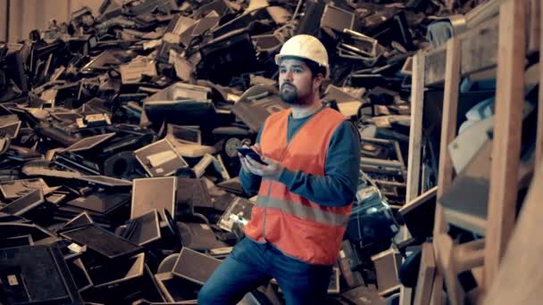 Trabajador de basurero con un teléfono inteligente está de pie cerca de una pila de basura — Vídeos de Stock