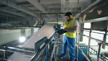Dizüstü bilgisayarı olan erkek işçi kağıt üretim makinesini inceliyor. Mühendis, fabrika işçisi..