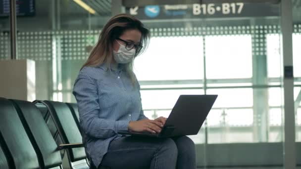 Sala de partida e uma senhora com uma máscara médica usando um laptop — Vídeo de Stock