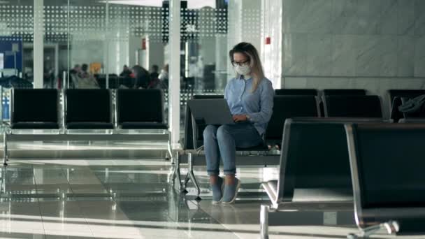 Repülőtéri társalgó egy hölgy visel orvosi maszkot, és egy laptop — Stock videók