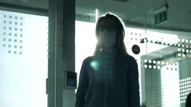 Bakgrundsbelyst kvinna i medicinsk mask filmas genom glaset. Coronavirus, epidemi och pandemi. — Stockvideo