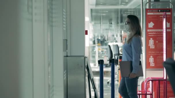 Une dame avec un masque de sécurité est debout dans un salon de départ avec un ordinateur portable — Video