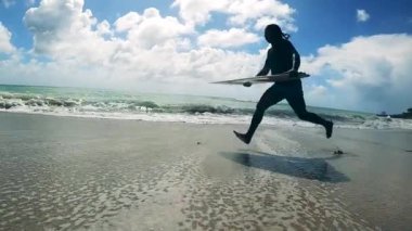 Tanımlanamayan adam sahildeki sörf tahtasından koşuyor ve düşüyor.