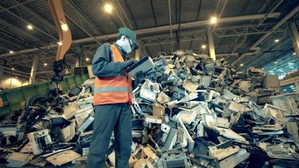 Un montón de equipo roto en un vertedero con un trabajador masculino. Basura, residuos, centro de reciclaje de basura . — Vídeo de stock