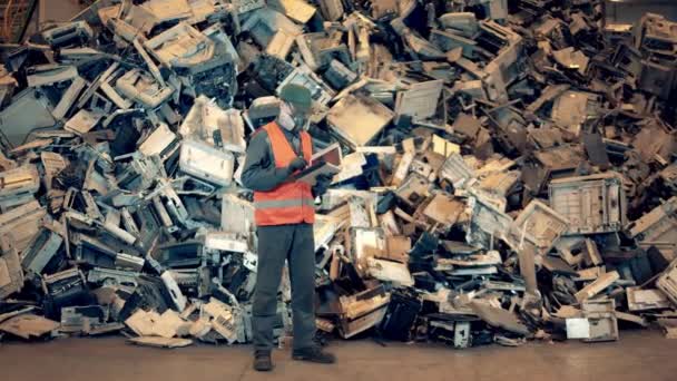 Trabalhador do sexo masculino numa unidade de ferro-velho com uma pilha de equipamento defeituoso. Lixo, fábrica de reciclagem de plástico . — Vídeo de Stock