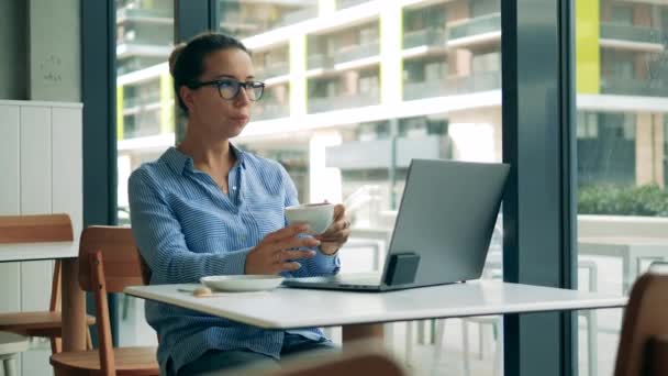 Prachtige dame drinkt koffie en werkt aan een laptop — Stockvideo