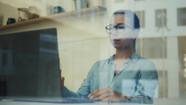 Affärskvinna som arbetar på en bärbar dator filmas genom fönstret — Stockvideo