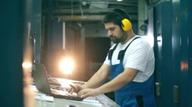 Mühendis bir fabrika biriminde planlar ve bilgisayarlarla çalışıyor.