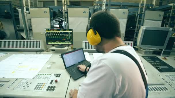 Ingeniero de fábrica de papel está escribiendo en un ordenador portátil en una vista trasera — Vídeos de Stock