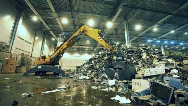 Indoors dumpsite with electronics debris and an excavator — Stock Video