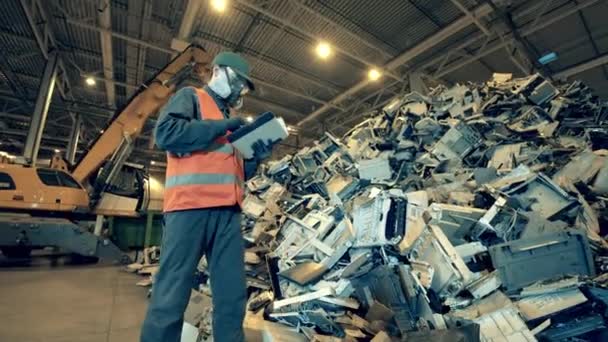 Avfallsinspektör med en tablett som observerar en hög med avfall. Elektronisk sopåtervinningsfabrik. — Stockvideo