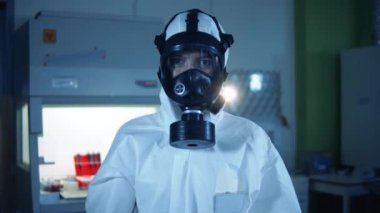 Tehlikeli madde giysisi giymiş bir laboratuvar çalışanı kovid 19 test tüpü gösteriyor. Epidemiyoloji uzmanı Coronavirus COVID-19 numuneleri üzerinde çalışıyor. Küresel Salgın Konsepti.