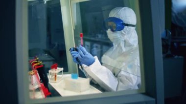 Tehlikeli madde giysisi giyen kadın uzman test tüplerini inceliyor.