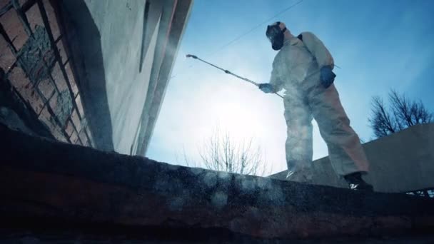 En person i skyddsdräkt sprutar kemikalier på en vägg. — Stockvideo
