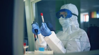 Sıçrama kıyafeti giymiş kadın bir laboratuar çalışanı test tüpünü inceliyor.