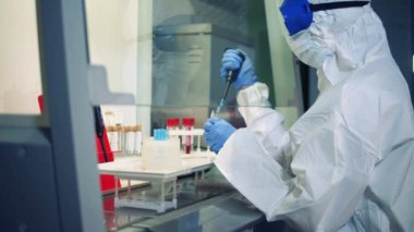 Tehlikeli madde giysisi giymiş bir araştırmacı kimyasallarla çalışıyor.