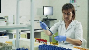 Kadın laboratuvar çalışanı test tüpleri arasında biyolojik örnekler taşıyor.