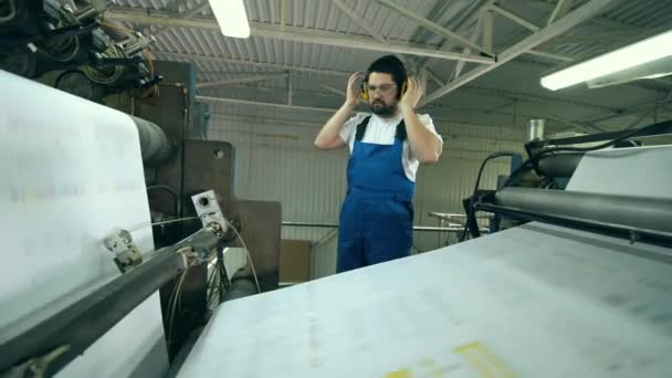 Fabrikstekniker inspekterar papper rullande genom maskinen — Stockvideo