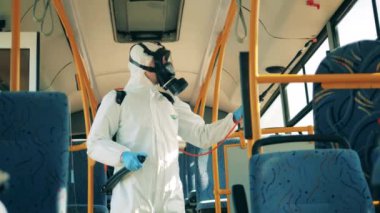Tehlikeli madde giysisi giymiş biri otobüsün içini dezenfekte ediyor. Coronavirus önleme, dezenfeksiyon süreci.