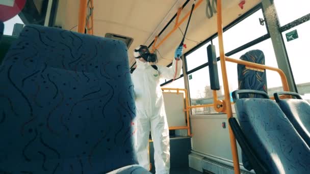 Una persona con un traje de salpicadura está desinfectando el autobús desde dentro. — Vídeo de stock