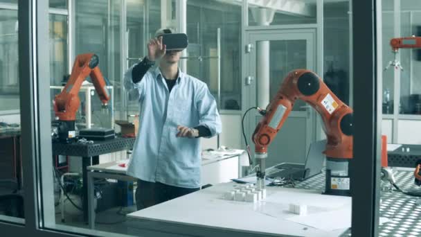 Мужчина-исследователь в VR-очках в лаборатории с роботом — стоковое видео