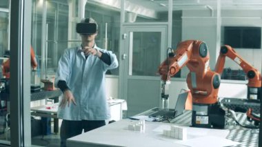 Genç bilim adamı sanal gerçeklik yoluyla bir robotu yönetiyor. VR kulaklık takan ve laboratuvarda robot mühendisliği projesinde çalışan bir adam..