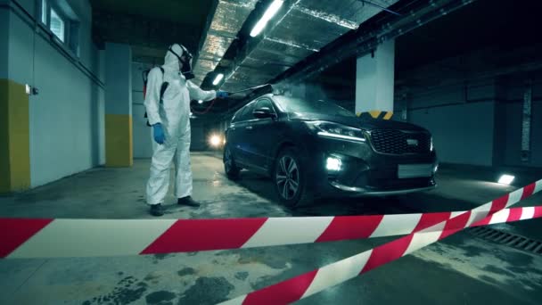 Una persona en traje de materiales peligrosos está desinfectando químicamente un coche — Vídeo de stock
