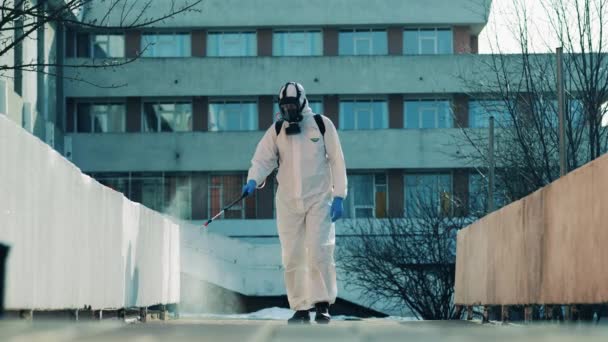 Expert in a hazmat suit is disinfecting concrete walls in the street — Stock Video