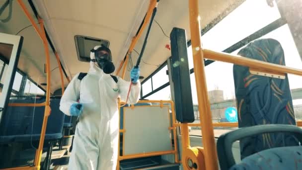 A person in a hazmat suit is chemically decontaminating the bus. Person in protective suit sprays chemicals, disinfectant. — Stock Video