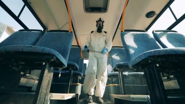 コロナウイルスの予防、流行の概念。消毒の専門家はバスに沿って歩いていて消毒しています — ストック動画