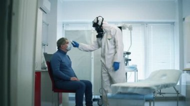 Koruyucu giysili sağlık görevlisi hastaların sıcaklığını ölçüyor. Koronavirüs hastasının yanında koruyucu doktor var..