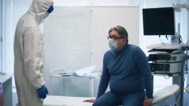 Tehlikeli madde giysisi içindeki doktor yaşlı bir adamın sıcaklığını ölçüyor. Hasta Coronavirus hastası, hastanede, covid-19 konsepti..