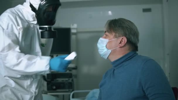 Doktor používá pyrometr na staršího pacienta. Sick coronavirus patient in a hospital, covid-19 concept. — Stock video