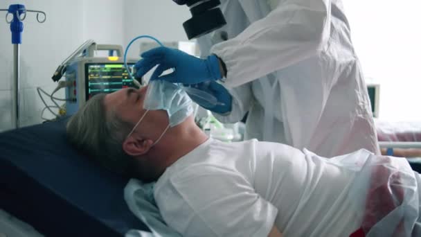 Paramedicus zet een zuurstofmasker op een mannelijke patiënt. Coronavirus, covid-19 geïnfecteerde patiënten in een kliniek. — Stockvideo