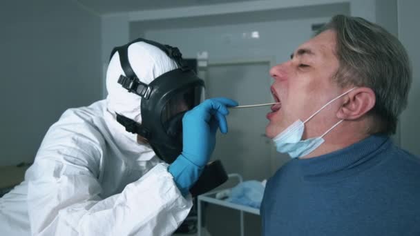 Spezialist in einem Schutzanzug kontrolliert den Hals des Patienten. Arzt in schützender Nähe von Coronavirus-Patient. — Stockvideo