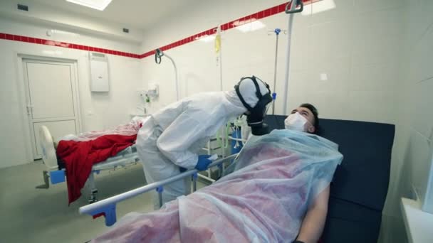 Врач в защитном костюме проверяет температуру лежащего пациента. Ковид-19, пандемическая, вирусная, коронавирусная болезнь, мировая, коронавирусная инфекция . — стоковое видео
