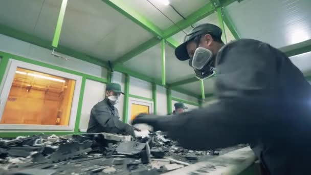 Junkyard werknemers sorteren fragmenten van afval op een transportband — Stockvideo