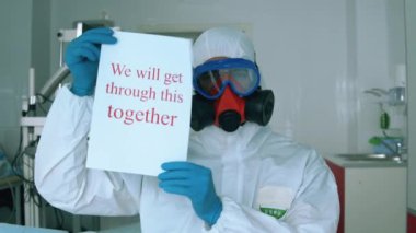 Tehlikeli madde giysisi içinde bir hastane çalışanı cesaret verici bir poster gösteriyor.