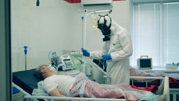Ένας γιατρός με προστατευτική στολή δίνει σε έναν ασθενή ενδοφλέβια κατά τη διάρκεια πανδημίας. Ιός του Coronavirus, ασθενής με covid-19 σε μονάδα εντατικής θεραπείας σε νοσοκομείο. — Αρχείο Βίντεο