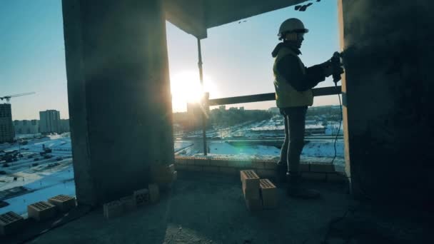 Un travailleur masculin est en train de tamponner un mur d'un immeuble à plusieurs étages en cours. Travailleur de la construction sur un chantier . — Video