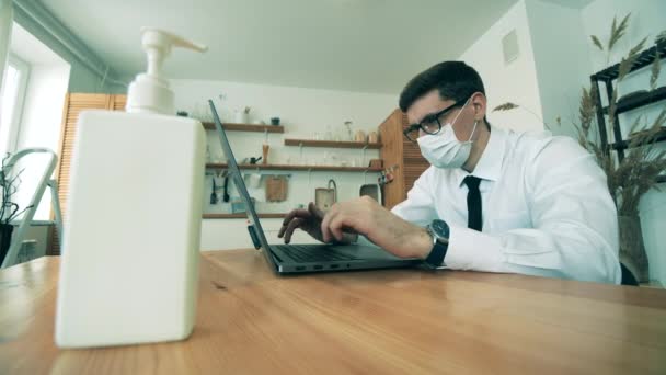 El hombre de negocios está desinfectando las manos mientras trabaja en una computadora portátil desde casa. Trabajo de hombre en casa en cuarentena durante brote de covidio-19 . — Vídeos de Stock