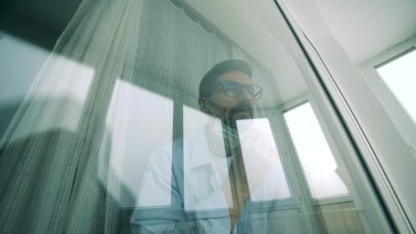 Een man doet een medisch masker op terwijl hij door het raam kijkt tijdens een pandemie van het Coronavirus, covid-19 uitbraak.. — Stockvideo